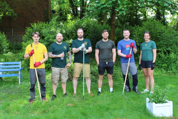 Volunteer group stood in a row, holding gardening tools